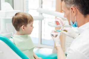 Dentist educating little boy about brushing teeth in clinic